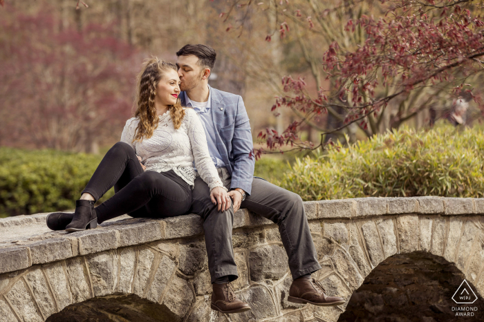 Sesja fotograficzna dla par stylu życia w Richmond w stanie Wirginia w Maymont Gardens, pokazująca kochanków siedzących na łukowatym kamiennym moście