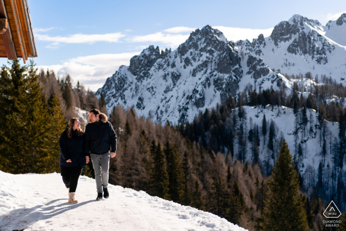 Tarvisio untraditionelles Lifestyle-Engagement-Porträt eines Paares, das zusammen im Winterschnee am Monte Lussari in Udine, Italien, spazieren geht