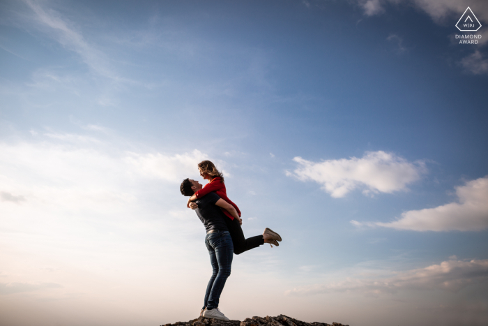 Immagine pre-matrimonio Chapelle de Dourgne | Tarn, Francia Sessione d'amore, mentre prende in braccio la sua fidanzata contro un cielo azzurro con nuvole bianche