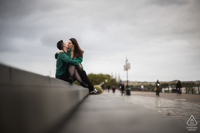 Retratos de compromiso de Burdeos para una pareja sentada en un bordillo de hormigón en una escena urbana en Francia