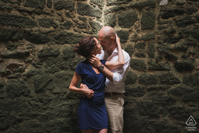 Pre wedding picture of the couple embraced under a shaft of light near a stone wall in Finistère, France