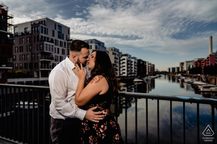 A Frankfurt couple posing and kissing above the calm, flat waters on Main river