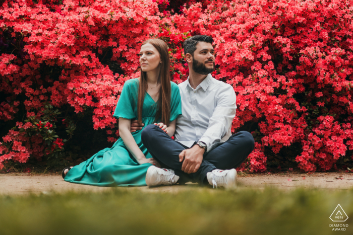 At the Botanical Gardens, a couple is sitting on the ground in front of flowers