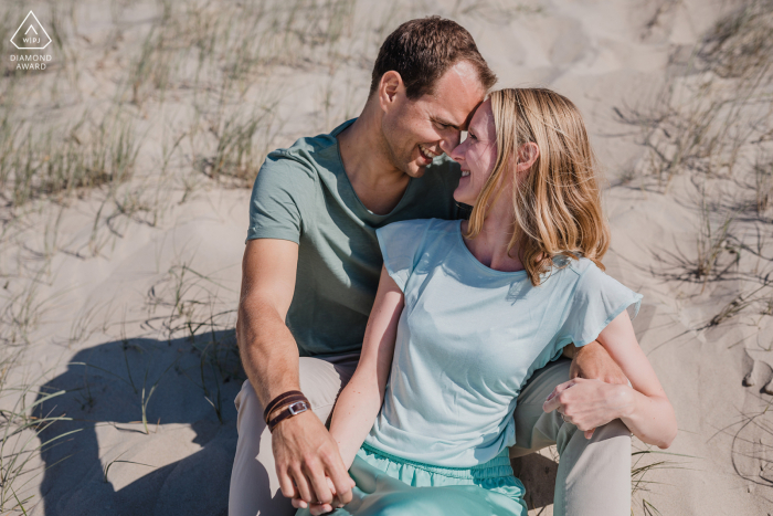 The couple is sitting at the beach in the sand while touching heads together In Domburg, the couple is sitting at the beach in the sand while touching heads together