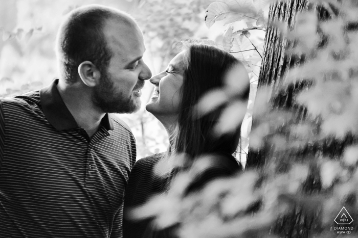 couple is laughing after a kiss in the woods during a BW portrait shoot At Pine Lake, GA, a couple is laughing after a kiss in the woods during a BW portrait shoot