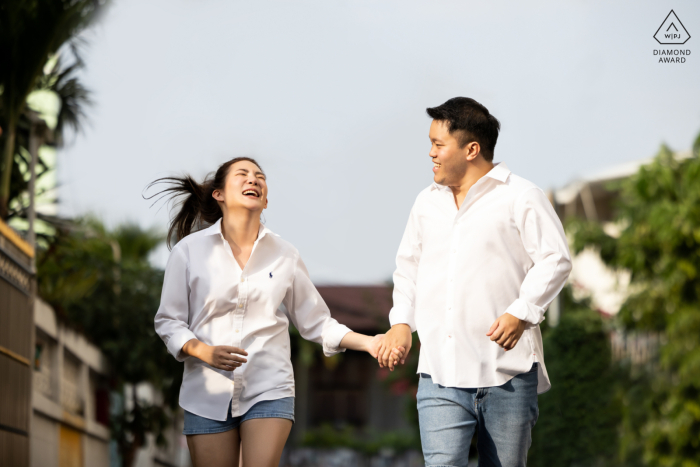 Una pareja corre y ríe mientras el viento sopla su cabello bajo el brillante cielo azul durante su sesión de retratos en Bangkok.