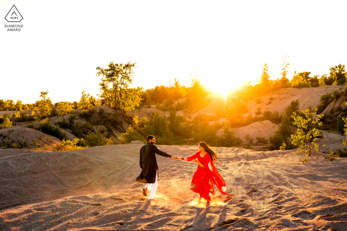 The couple's engagement portrait captures the romantic moment of them dancing in the Manitoba, Canada sunset, the red dress twirling in the golden sunlight