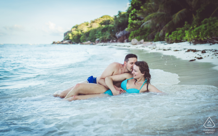 A couple enjoys a pre-wedding beach portrait session at Anse Gaulette in La Digue, Seychelles, as they relax in the waves lapping on the shore