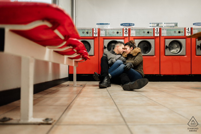 An engagement portrait in Chartres depicts a couple cuddling on the floor of a laundromat, beautifully captured from a low angle perspective
