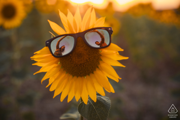 A couple in Lectoure, Gers, France, smiles and gazes at each other while their reflection is beautifully captured in the sunglasses they are wearing