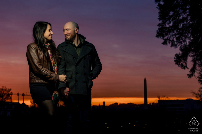 Um casal prestes a se casar posou para sua sessão de retratos de noivado em Washington DC, com o pôr do sol iluminando-os lindamente enquanto o fotógrafo capturava o icônico monumento de Washington ao fundo.