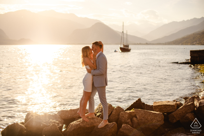 Loving Embrace: Stunning Sunset Portrait of Elegant Couple at Lake Maggiore, Italy Lifestyle couple portrait at Lake Maggiore, Italy captures a lovely couple in light earthy colors, kissing on a rock jetty by the water at sunset.