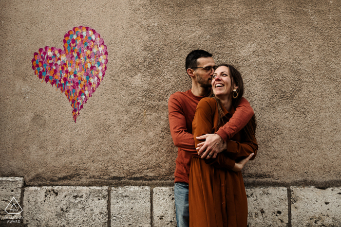A couple embraces in the middle of the street with graffiti art heart painted on the wall behind them. A fine art portrait by a Chartres wedding photographer.