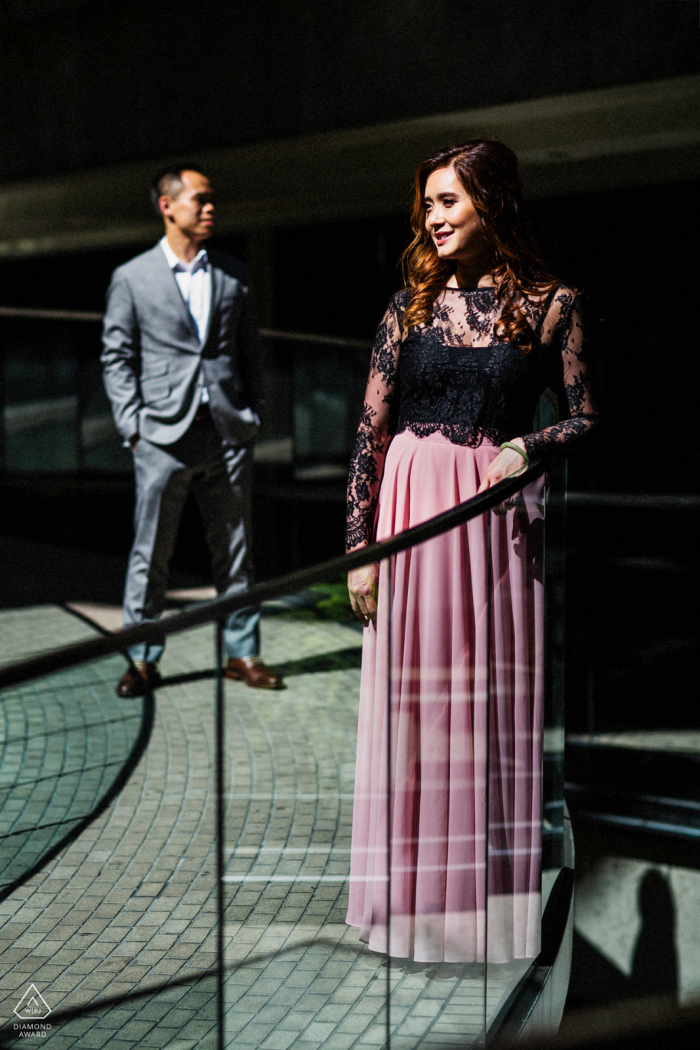 A couple portrait taken in the city by a North California wedding photographer, showcasing a creative composition with sunlight filtering through a glass panel railing with geometric curves and shadows in San Francisco.