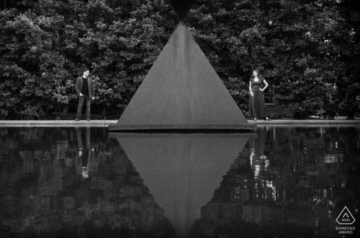 Engaged couple stands in reflection pool at Houston's Rothko Chapel, framed by the iconic Barnett Newman's Broken Obelisk sculpture.