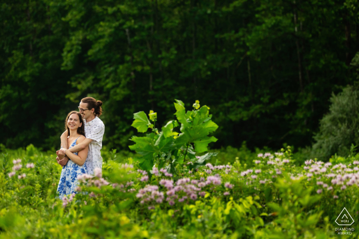 WPJA professional captures an engaged couple in a scenic Frenchtown, NJ garden, as the groom wraps his arms around his fiancée amidst the vibrant green foliage.