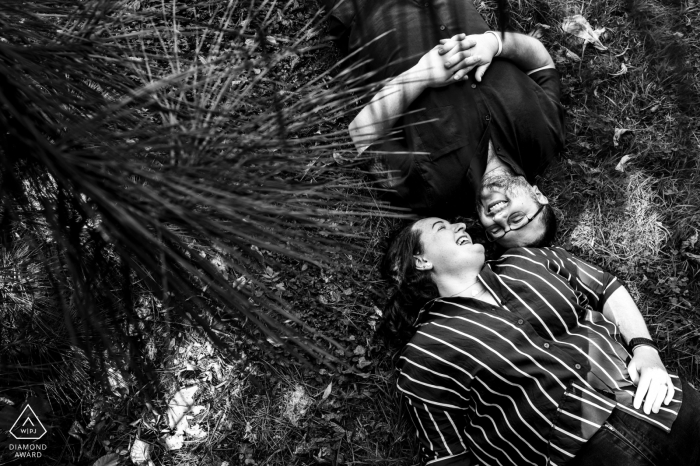 In the town of Nancy, France, the photographer showcases a playful and relaxed manner in the artistic engagement portrait of a laughing couple lying on the ground.