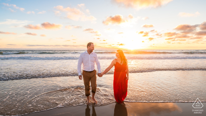 Beachside Serenity: Engaged Couple's Hand-in-Hand Moment Amidst Gentle Tide at Lège-Cap-Ferret, France - A Romantic Engagement Portrait In Lège-Cap-Ferret, France, an engaged couple stands hand in hand for a beach session. Center framed, the gentle tide washes over their feet.