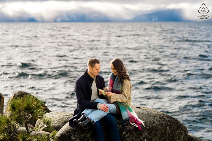Couple at Lake Tahoe, NV, Shares Intimate Engagement Session on Boulders | Reading Notes to Each Other Creates Heartfelt, Memorable Experience At Lake Tahoe, NV, a couple shares an intimate session sitting on boulders along the shoreline. During their engagement session, they read a note to each other, creating a heartfelt and memorable experience.