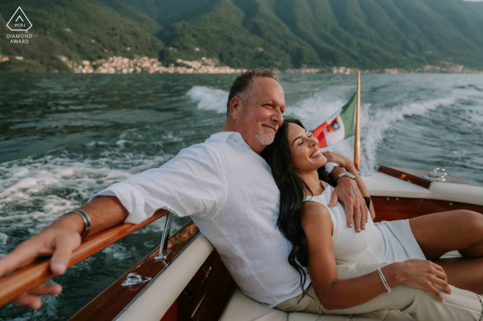 A newly engaged couple enjoys a peaceful boat ride on the serene waters of Lake Como, Italy, soaking in the beauty of the landscape as they relax together.