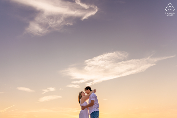 At Sandy Neck Beach, Sandwich, Massachusetts, a couple embraces warmly, surrounded by soft, dreamy clouds and the golden glow of the setting sun, epitomizing timeless love and unity.