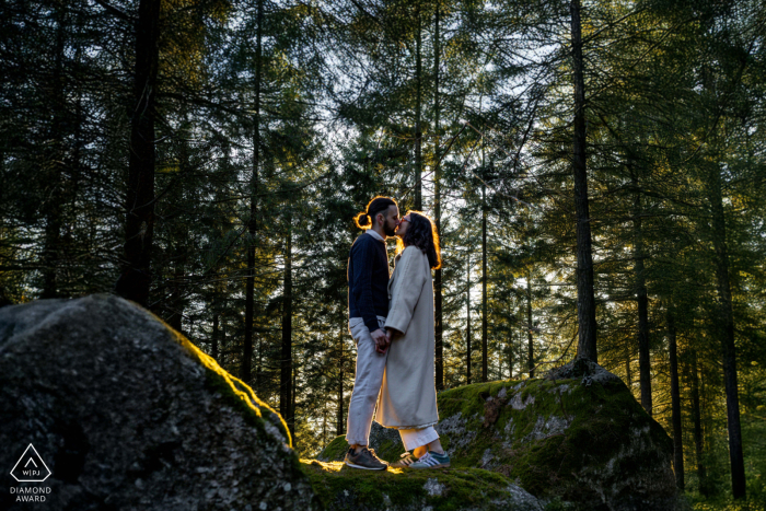 In the forest at Carnaval de Pierres, Uchon, a couple stands on a rock, beautifully backlit by the low sun filtering through the trees.