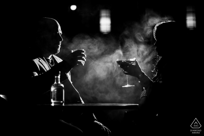 A black and white engagement portrait of a couple sharing a drink in Toronto's Kensington Market.