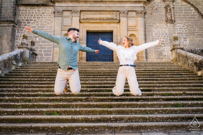 A joyful pre-wedding portrait in Baeza, Spain, captures a couple leaping from aged stone steps.