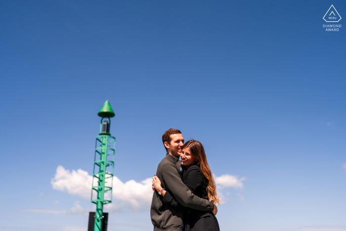Engaged couple posing under blue skies, tower visible beside them in Portopiccolo, Sistiana, Trieste, Italy.