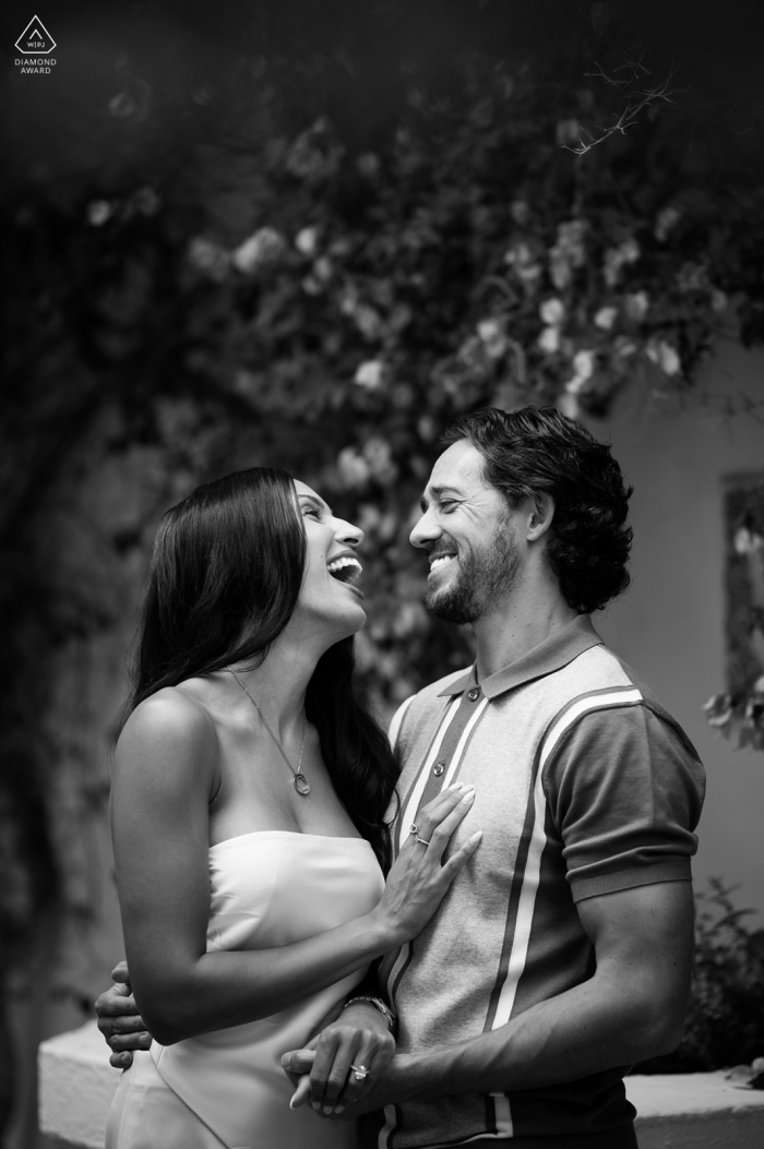 A newly engaged couple stands together beside lush foliage on the Marbella Club Pier, beaming with big smiles. The vertical black and white portrait captures their happiness after the surprise proposal.