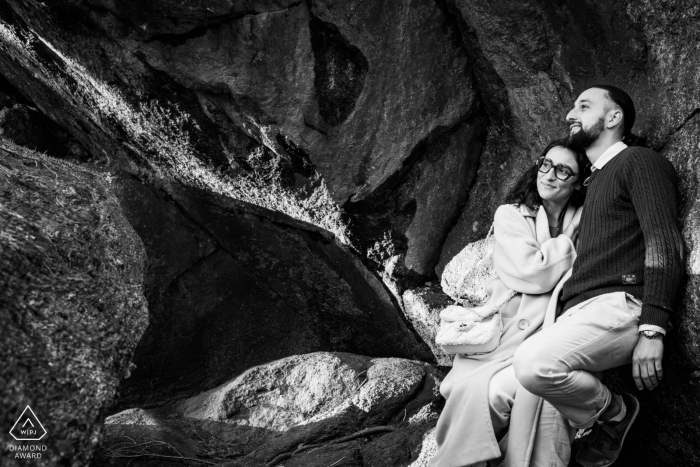 At Les Rochers du Carnaval, a couple relaxes together sheltered beneath the rocks in a black and white portrait. Their comfortable pose highlights a sense of intimacy and ease in the natural setting.