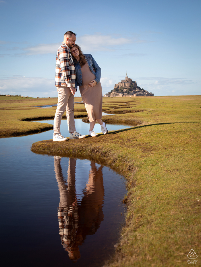 At Mont Saint Michel Bay, an expectant couple is framed vertically along the curving lines of the water’s edge, capturing the beauty of this location before their baby arrives.