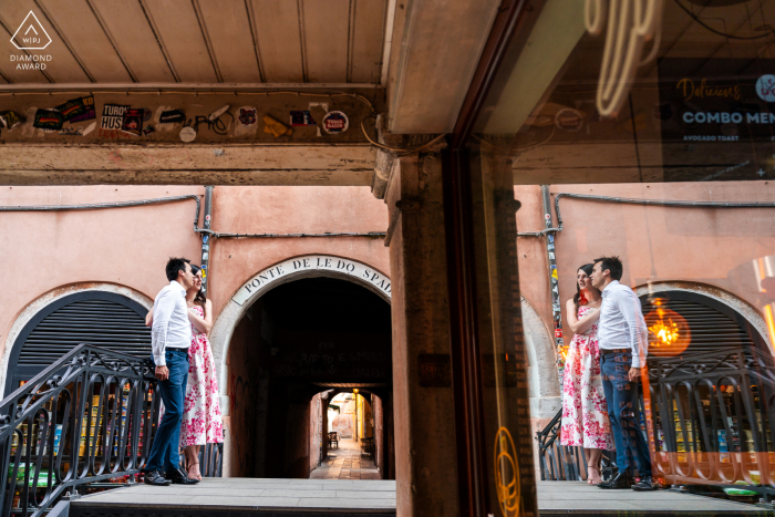 In Venice, Italy, the couple is beautifully captured with their reflection in a window, set against the backdrop of the city's iconic scenery.