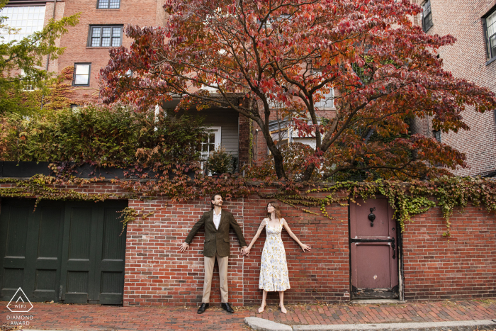 At Beacon Hill in Boston, Massachusetts, a couple holds hands while standing with their backs against a brick wall for a portrait.