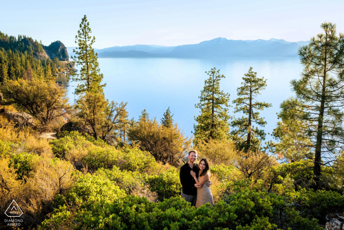 On a trail descending toward South Lake Tahoe in California, a couple poses together with the lake and surrounding natural landscape in the background during their engagement portrait session.