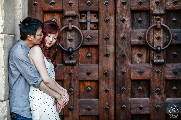 Napa in California - By a large old door, he wraps his fiancée in a gentle embrace from behind as they pose in profile for their engagement portrait in Napa, California.