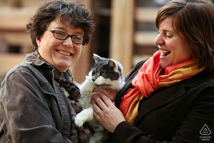 An engaged couple smiles as they hold their cat for a close-up portrait in Pine Lake, Georgia.