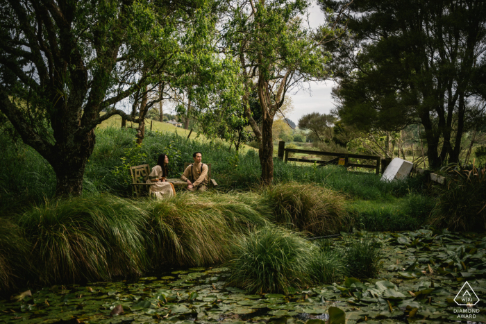 Couple Sits Chatting Quietly In Front Of Serene Lake Covered In Lilies In Wanaka New Zealand A couple sits chatting quietly in front of a serene lake covered in lilies in Wanaka, New Zealand, finding a peaceful and private connection in the beautiful outdoors.