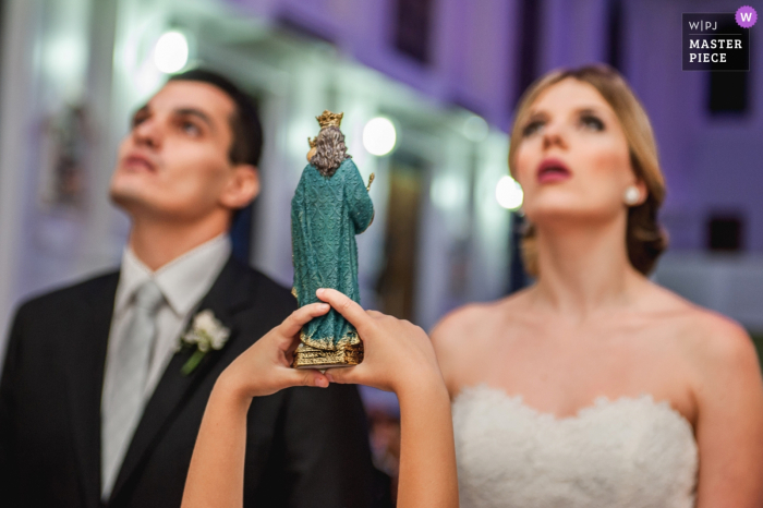 Brazil bride and groom look up as child holds a figure during the ceremony