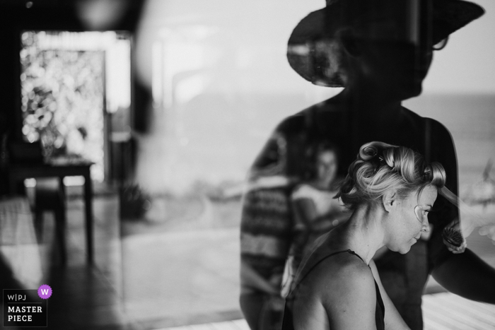 Photo: <a href="https://www.wpja.com/contests/2018-v01-photography-competition/best-wedding-photographers/2164301"> MangKhris Santika - Gianyar Bali </a> Le photographe de mariage de Bali a capturé ce reflet noir et blanc d'une épouse se coiffant pendant que quelqu'un regarde par la fenêtre