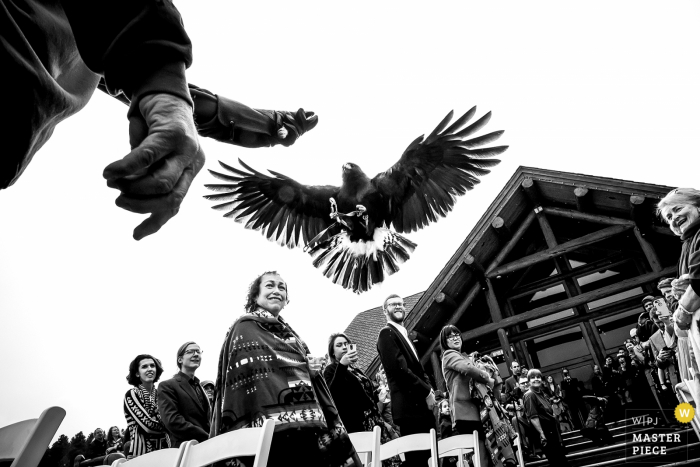 Photo by: <a href="https://www.wpja.com/contests/2018-v01-photography-competition/best-wedding-photographers/2164646">Jesse La Plante - Boulder Colorado</a> Boulder wedding photographer captured this black and white image of a falconer and his falcon outside of a log cabin during the wedding ceremony