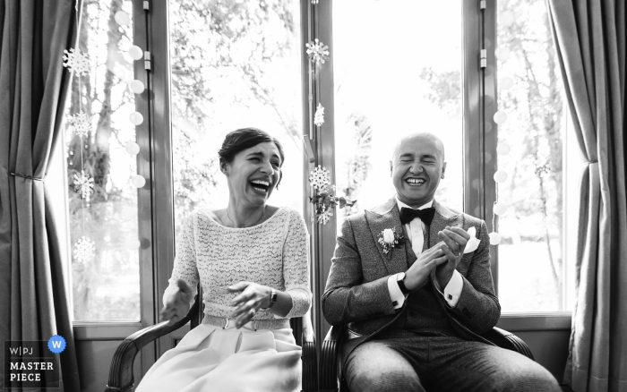 Der Hochzeitsfotograf aus Nouvelle-Aquitaine hat dieses Schwarz-Weiß-Porträt einer Braut und eines Bräutigams aufgenommen, die vor einem großen Panoramafenster lachen