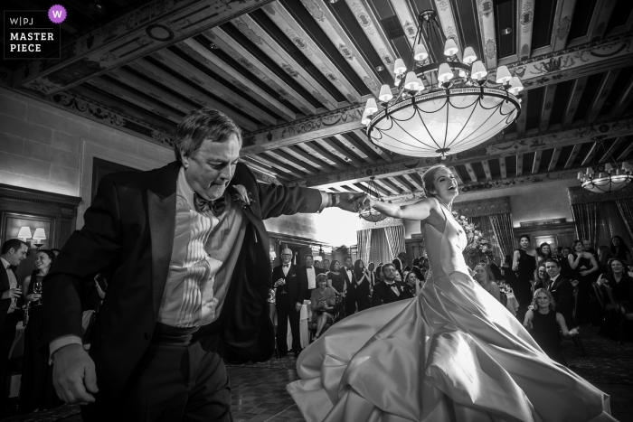 Detroit wedding photographer captured this black and white photograph of a lively father daughter dance under an exposed beam ceiling and large chandelier 