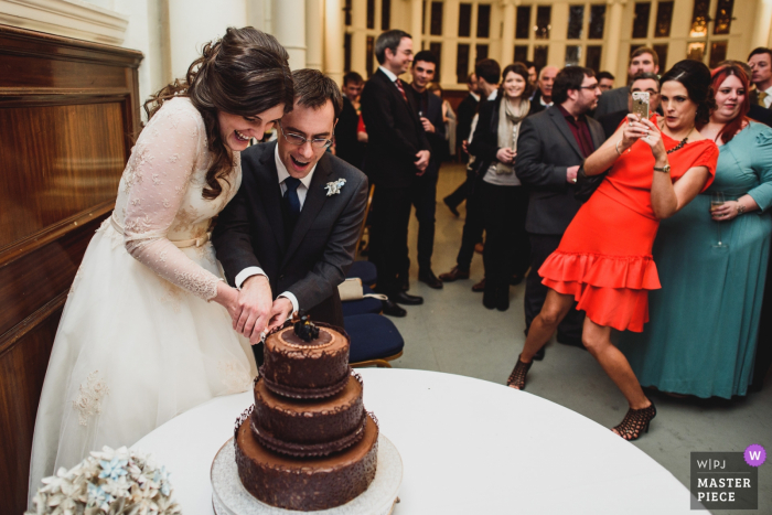 Photo by: <a href="https://www.wpja.com/contests/2018-v01-photography-competition/best-wedding-photographers/2170946">Mark Wallis - Belper Derbyshire</a> Old Finsbury Town Hall, London Wedding Photo of Bride and Groom Cutting Chocolate Cake