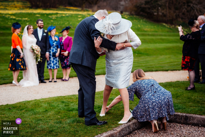 Photo by: <a href="https://www.wpja.com/contests/2018-v01-photography-competition/best-wedding-photographers/2174391">Emil Boczek - Wolverhampton West Midlands</a> Evesham guests helping a lady with her shoe while the bride and groom pose for a picture in the background