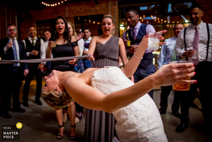 Photo by: <a href="https://www.wpja.com/contests/2018-v03-photography-competition/best-wedding-photographers/2185856">Victoria Sprung - Chicago Illinois</a> Chicago, Illinois bride holds her drinks and plays limbo at the same time at the wedding reception