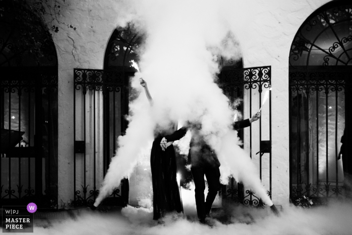 Foto door: <a href="https://www.wpja.com/contests/2018-v03-photography-competition/best-wedding-photographers/2186406"> Lukas Guillaume - Miami Florida </a> De bruid en de bruidegom van Miami, Florida houden handen en golf door de rook bij de huwelijksontvangst