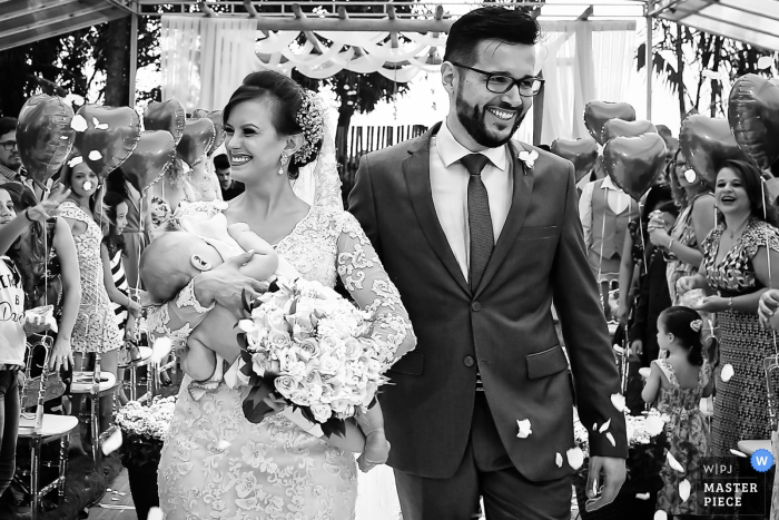 Goiania bride and groom walk down the aisle with the bride holding a baby