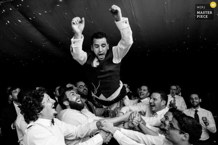 Foto por: <a href="https://www.wpja.com/contests/2018-v06-photography-competition/best-wedding-photographers/2208116"> Marianne Chua - Londres, Londres </a> Os hóspedes jogam o noivo para o ar na recepção do casamento no Braxted Park