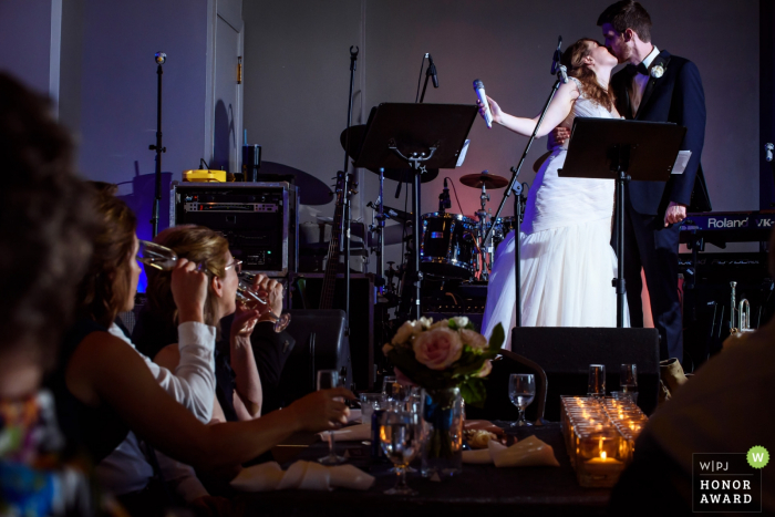 Photo by: <a href="https://www.wpja.com/contests/2018-v06-photography-competition/best-wedding-photographers/2210756">Janine Cooper - Omaha Nebraska</a> Omaha, Nebraska Wedding Photographer - the bride and groom kiss on stage after a toast
